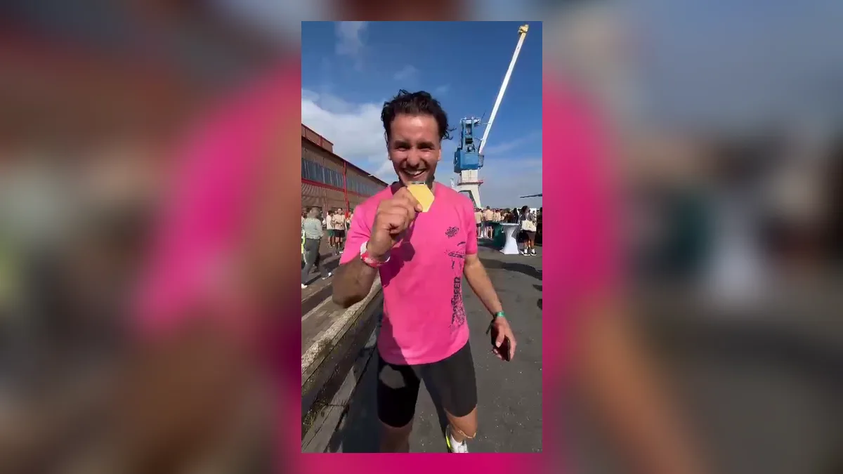 Ayoub Assaidi houdt lachend zijn medaille naar de camera, met havenkranen op de achtergrond
